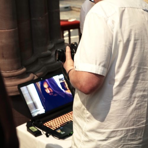 People looking at a computer screen that shows a close up of a cloaked monk.